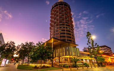 A round high-rise tower above a lit glass-fronted building at dusk