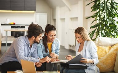 An agent going through a folder of documents with a couple on a sofa in their living room