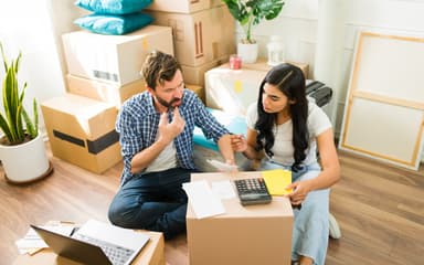 A couple sitting among moving boxes going through bills with a calculator and a laptop