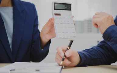 An adviser holding up a calculator across a desk while a client takes notes