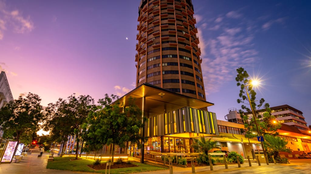 A round high-rise tower above a lit glass-fronted building at dusk