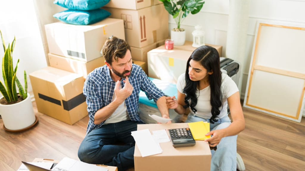 A couple sitting among moving boxes going through bills with a calculator and a laptop