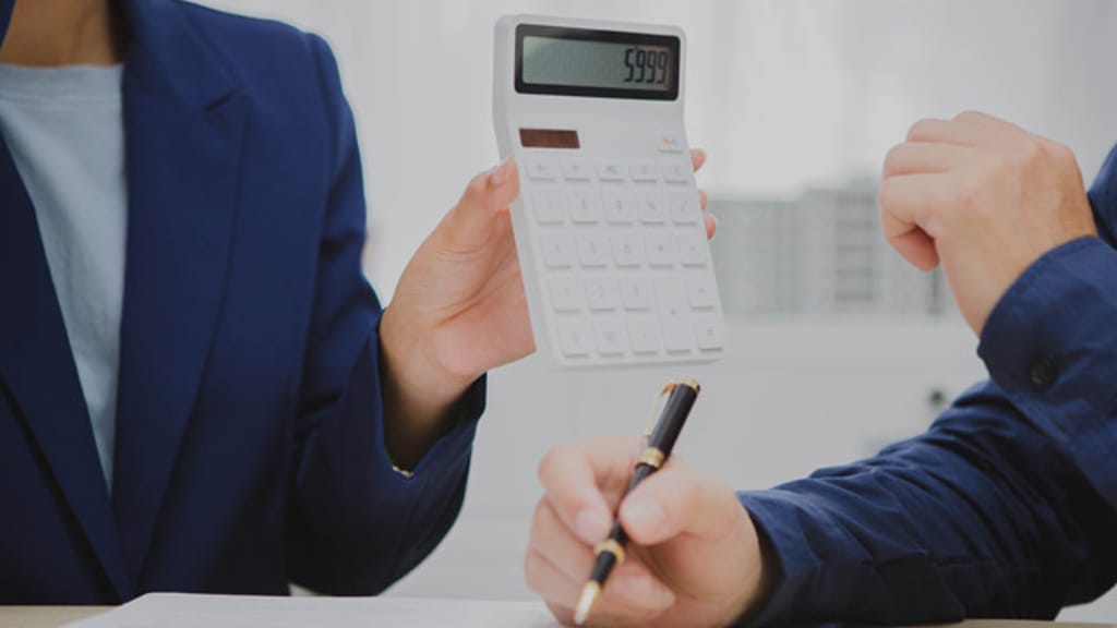 An adviser holding up a calculator across a desk while a client takes notes