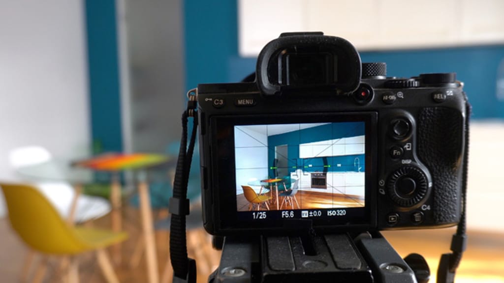 A camera on a tripod framing a kitchen and dining room through its rear screen